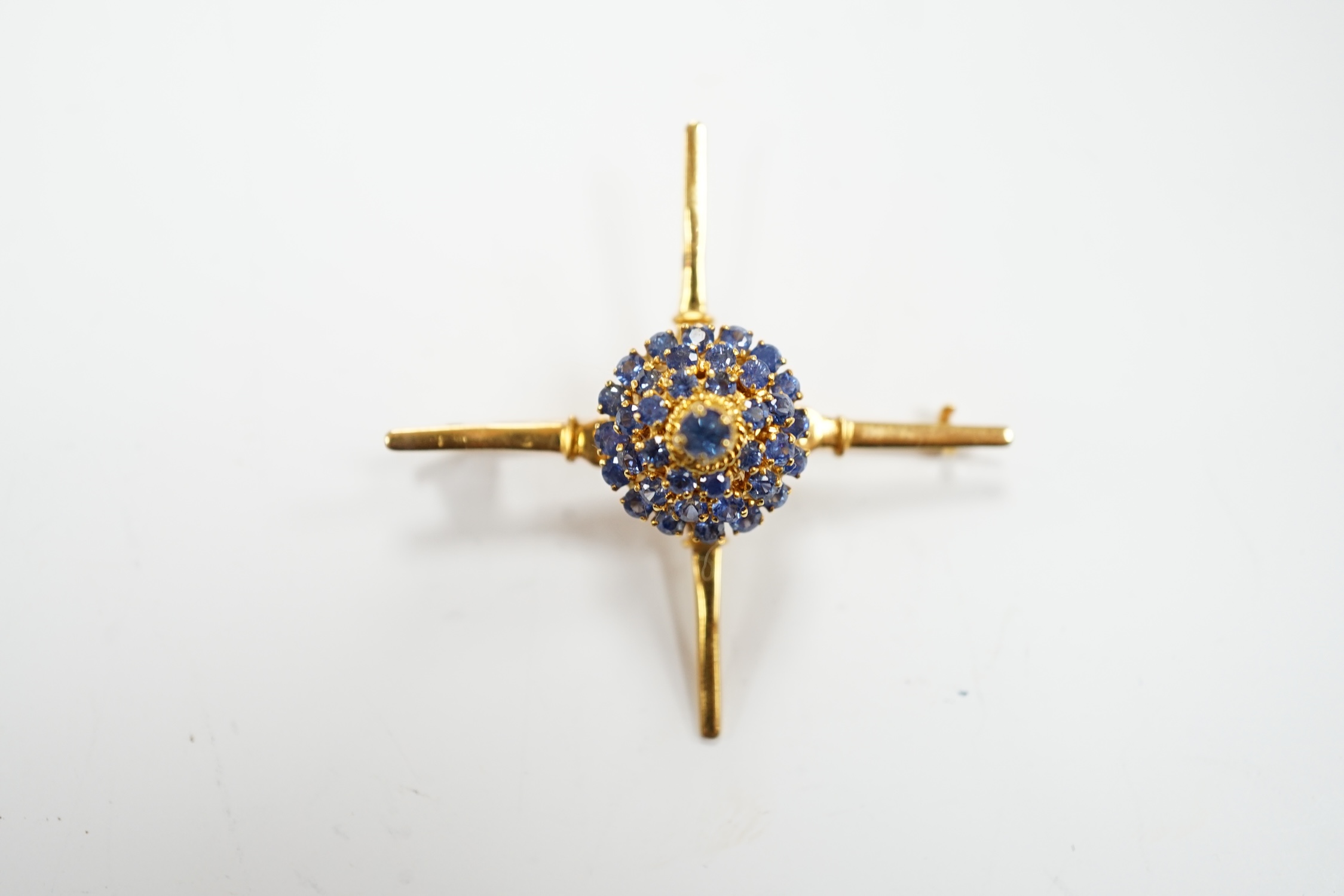 A yellow metal and sapphire cluster set brooch, of 'X' form with raised central motif, 45mm, gross weight 6.2 grams.